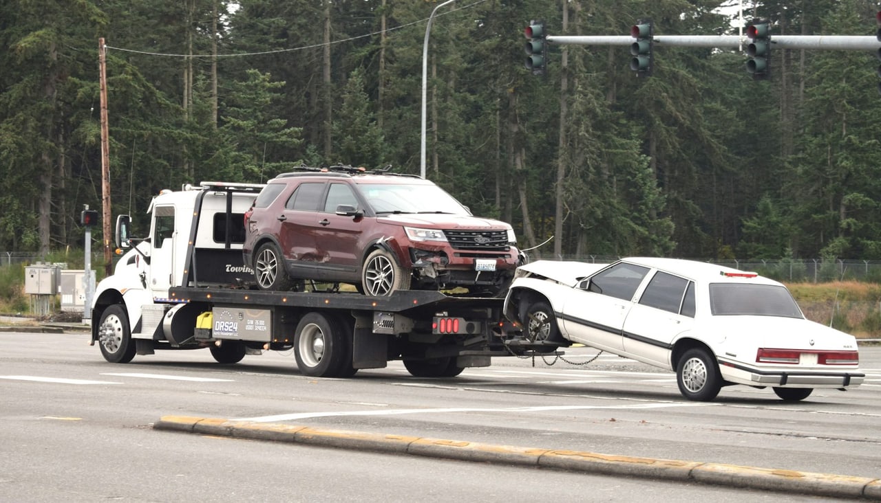 Flatbed tow truck loading a wrecked car at an intersection, illustrating towing cost in Lake County FL