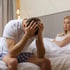 Man distressed on bed, woman behind him, depicting Erectile Dysfunction issues.