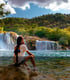 Eine Person sitzt auf einem Felsen und blickt auf einen breiten Wasserfall und einen See m Naionalpark Krka.