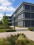 Modernes Bürogebäude mit großen Fenstern und Außenjalousien, umgeben von gepflegten Grünflächen und Gehwegen.