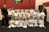 Eine Gruppe Kinder in weißen Karate-Anzügen hält Zertifikate; zwei erwachsene Trainer stehen daneben.