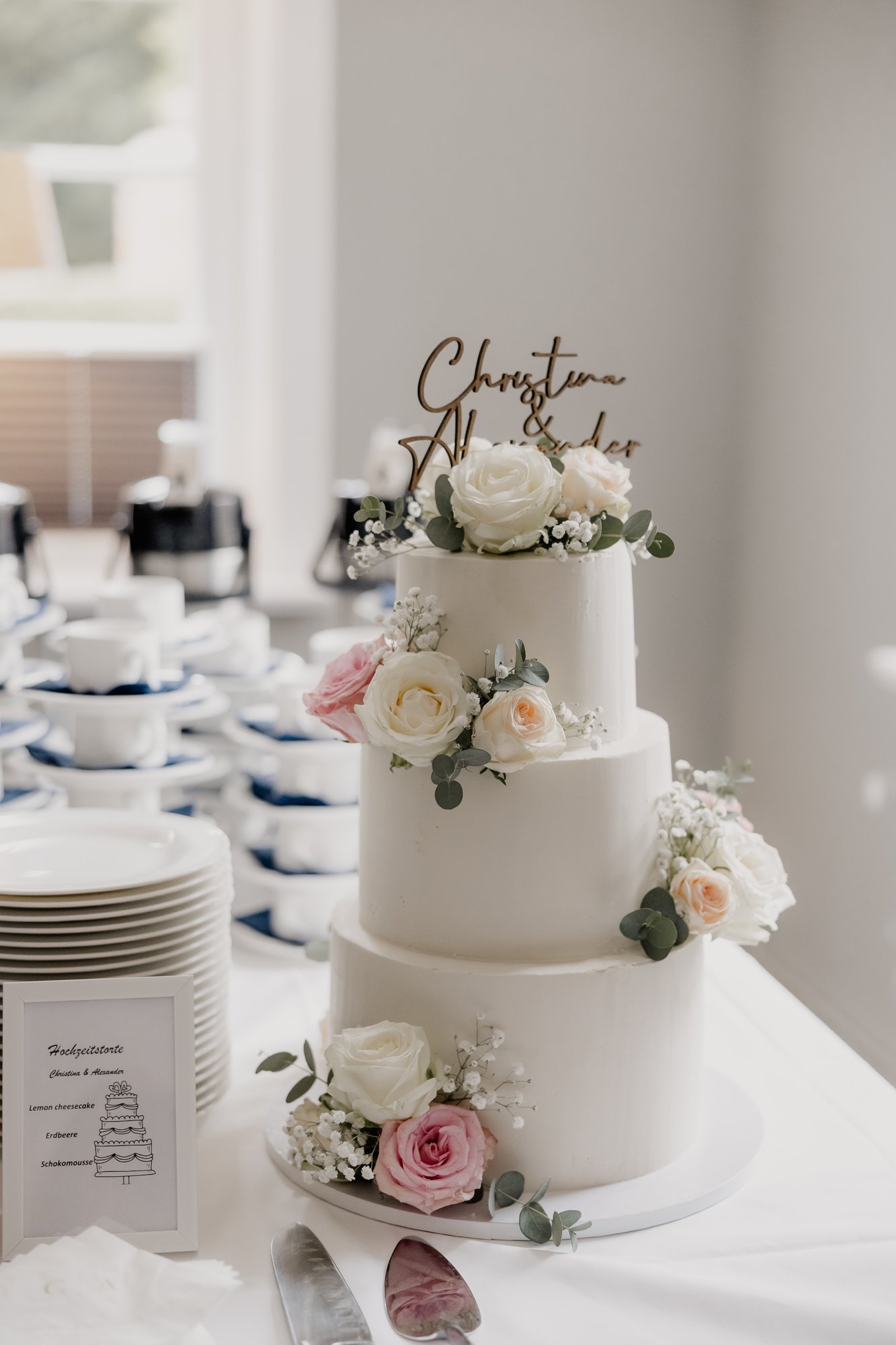 Hochzeitstorte mit weißen und rosa Rosen neben dem gedeckten Kaffeetisch
