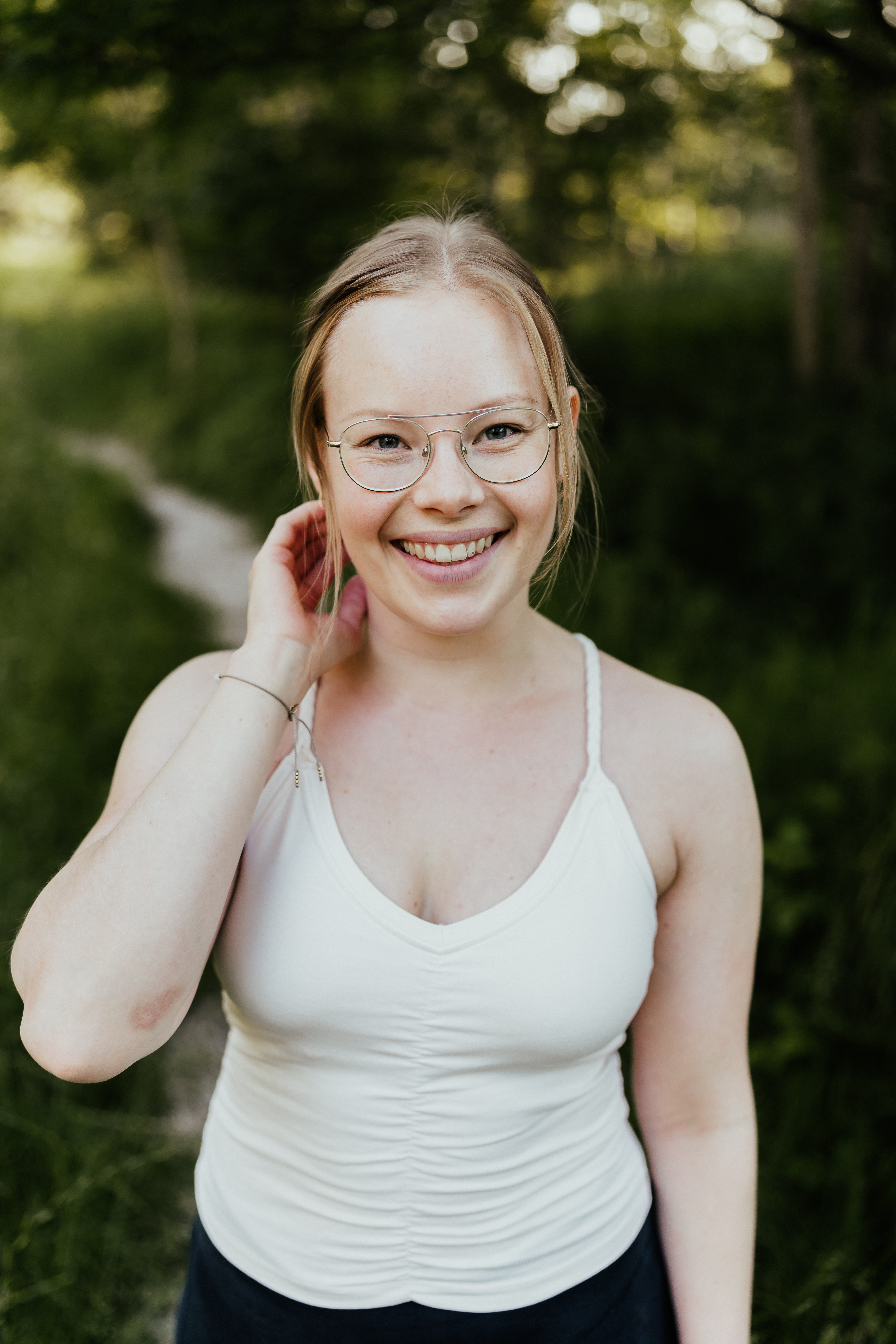 Anna-Maria Köstler, Yogalehrerin und Coach für feinfühlige Frauen, freundlich lächelnd vor grünem Wald-Hintergrund.