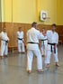 Mehrere Personen in weißen Karate-Anzügen und schwarzen Gürteln üben in einer Turnhalle.