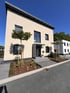 Modernes Einfamilienhaus mit beiger Fassade, Pultdach und gepflegtem Vorgarten unter blauem Himmel.