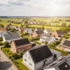 Luftaufnahme einer Wohnsiedlung mit Häusern, die Photovoltaikmodule auf den Dächern haben, unter sonnigem Himmel.