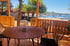 Holzveranda mit Tisch und Stühlen, Blick auf eine Bucht mit Booten und Gebäuden.