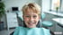 Ein lächelnder Junge mit blonden Haaren sitzt mit einem hellblauen Patientenservietten-Latz auf einem Zahnarztstuhl.