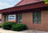 The brick exterior of Optima Medical General Practice with a sign on the wall and green bushes in front.