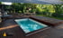 Rechteckiger Pool mit blauer Abdeckung und Holzdielen, umgeben von einem Garten mit Bäumen und Liegestuhl.
