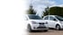 Zwei weiße Elektro-Kleinwagen, ein Seat Mii electric und ein Mitsubishi i-MiEV, parken nebeneinander im Freien.