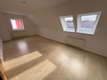 Leeres Dachgeschosszimmer mit zwei Dachflächenfenstern und Sonnenlicht auf dem Boden