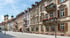 Gepflasterte Straße vor einer Reihe bunter historischer Gebäude mit Balkonen und Fenstern, im Hintergrund eine Kirche.