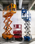 Drei Scherenhebebühnen in Orange, Rot und Blau stehen in einem Raum mit Betonwänden und -decken.