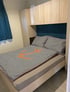 Bett mit schwarz-weiß gestreifter Bettwäsche und orangefarbenem Ankermotiv in einem Raum mit hellen Holzschränken und blauen Vorhängen.