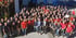 Große Gruppe von Mitarbeitern in blauen und roten Poloshirts vor einem Gebäude.