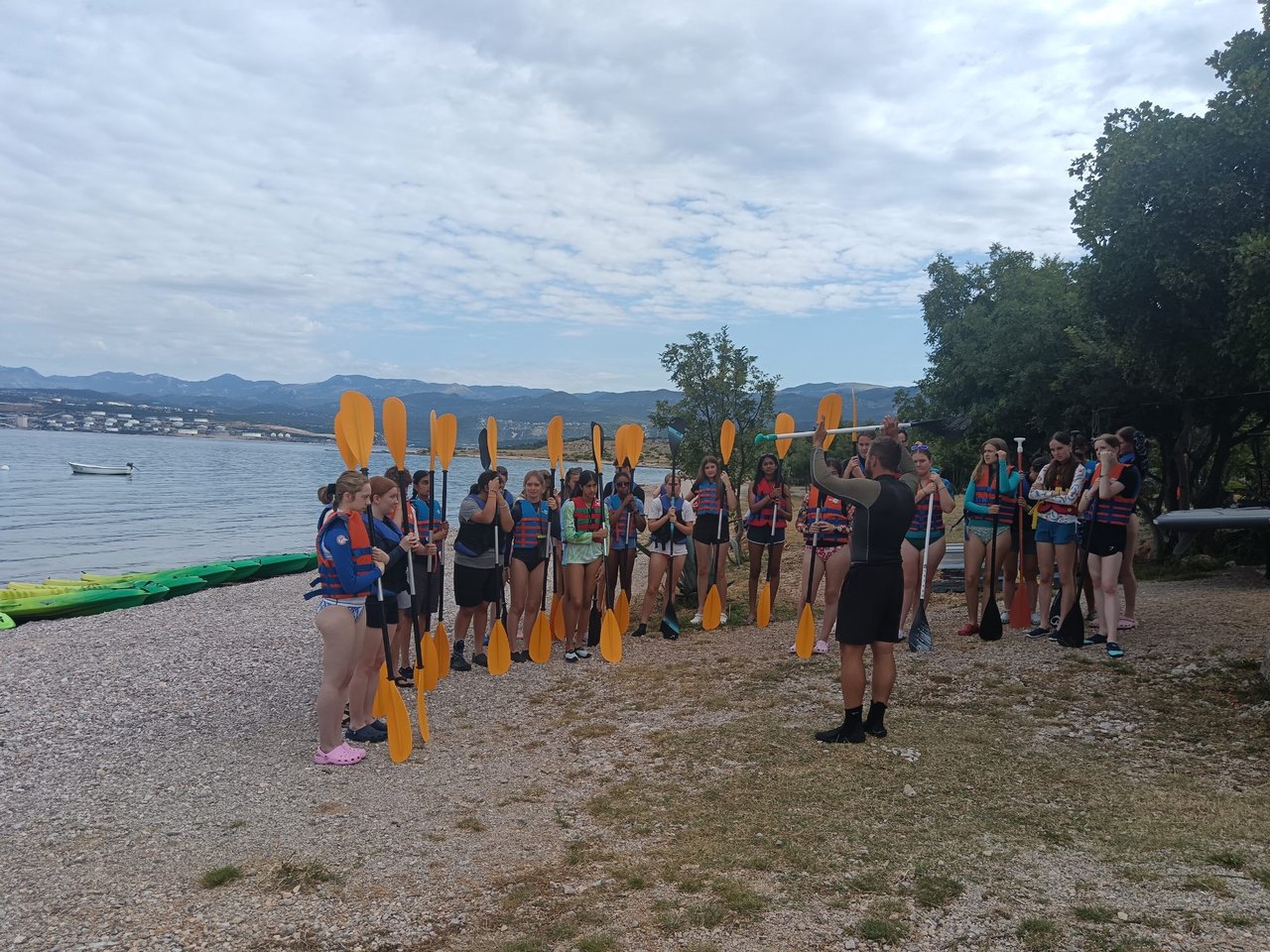 A large group standing on the beach holding paddles before a tour