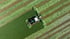 Grüner Traktor mit Mähwerk mäht ein Feld mit Streifen aus gemähtem und ungemähtem Gras.