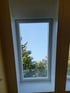 Dachfenster in einem Zimmer mit Blick auf blauen Himmel und grüne Bäume.