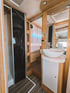 Badezimmer eines Wohnmobils mit Dusche, Waschbecken und Holzboden.