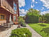 Modernes Holzhaus mit Terrasse, Gartenmöbeln und gepflegtem Rasen unter blauem Wolkenhimmel.