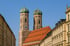 Die Frauenkirche in München mit zwei Zwiebeltürmen und roten Dächern zwischen Gebäuden.