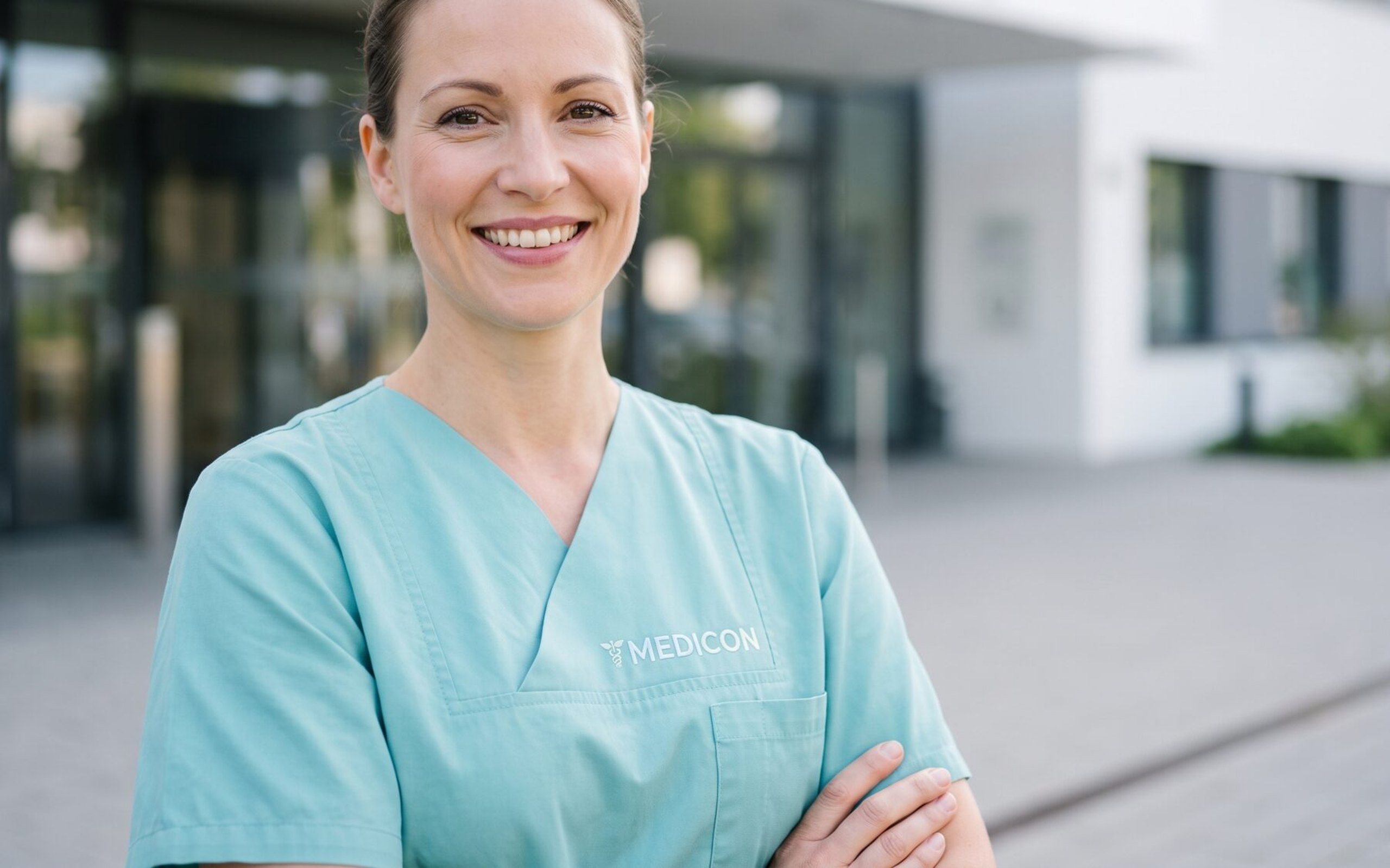 Pflegefachkraft im Medicon-Kasack vor dem Klinikeingang