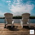 Two white Adirondack chairs on a wooden dock facing a calm lake under a partly cloudy blue sky.