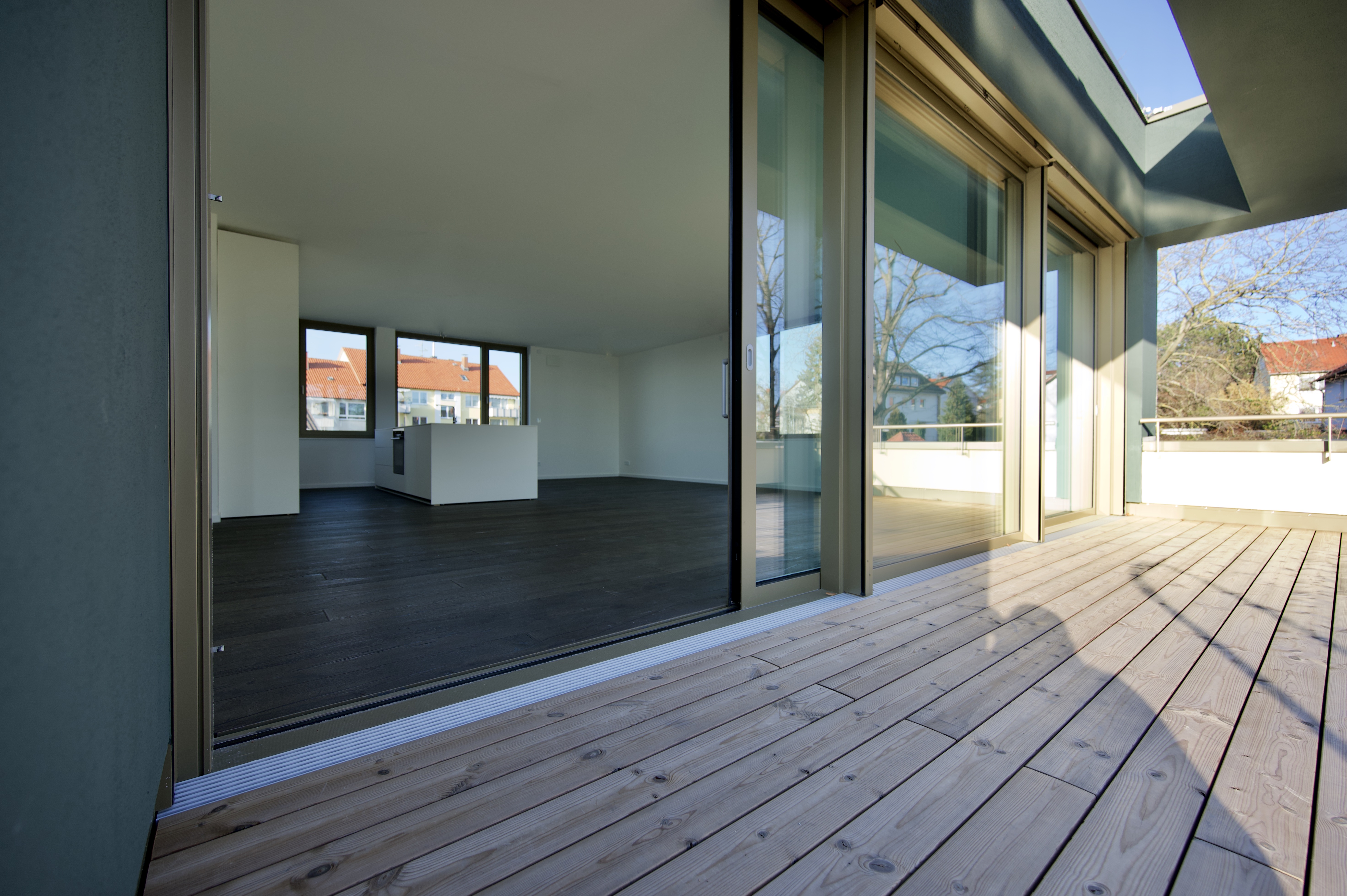 Großprojekt Himmelsruh – Holzterrasse vor großer Glasfront mit Blick in den Wohnraum