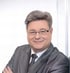 Portrait von Volker Pusch mit Brille und grauem Anzug lächelt, verschränkte Arme, lehnt an einer hellen Wand. Es handelt sich um den Gründer von der Anmara Hotline für Spirituelle Beratung und Coaching per Telefon und Chat