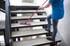 Reinigungsutensilien auf einem gelben Wagen neben einer weißen Treppe in einem hellen Flur.