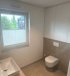 Modernes Bad mit Fenster, Waschbecken, Toilette und weißen Wandschränken.