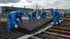Drei Arbeiter in blauen Schutzanzügen und Atemschutzmasken entfernen Wellblechplatten von einem Dach.