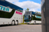 Zwei weiße Reisebusse mit grünen und pinken "Seitter" Logos stehen unter blauem Himmel.