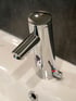 Ein glänzender, verchromter Wasserhahn mit Sensor und Temperaturregler über einem weißen Waschbecken.