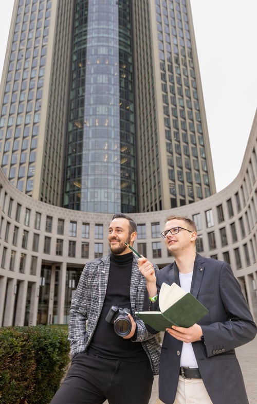 Lukas Wolf und Felix Mauersberger, Gründer von Visual Storytellers Leipzig, mit Kamera und Notizbuch vor einem Bürogebäude
