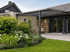 Moderne Terrassenüberdachung aus grauem Metall an einem Wohnhaus mit Garten, Natursteinwand und Loungemöbeln.