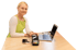 Frau mit grüner Schürze präsentiert ein Kartenzahlungsgerät neben Laptop und Smartphones auf einem Holztisch.
