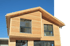Modernes Einfamilienhaus mit heller Holzfassade, Satteldach und großen Fensterfronten vor blauem Himmel.