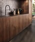 Modern kitchen with dark wood cabinets, black counter, integrated sink, black faucet, and stone-look backsplash.