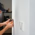 Mann in Kappe installiert Steckdose mit Schraubendreher an weißer Wand.