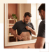 A man in a gray t-shirt looks in a bathroom mirror and pinches his stomach fat.