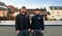 Zwei Solartechnik-Mitarbeiter in schwarzen Uniformen und Mützen stehen auf einem Dach mit Solarpaneelen.