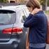 Woman holding her neck while looking at a dented car bumper and broken taillight.