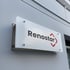 Ein beleuchtetes, mattweißes Schild mit dem schwarzen Schriftzug "Renostar" und einem roten Rauten-Logo an einer grauen Wand.
