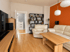 Modernes Wohnzimmer mit weißem Ledersofa, Holztisch, dunkelbraunem Regal und einer orangefarbenen Akzentwand.