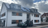 Modernes, weißes Wohnhaus mit Solarpaneelen auf dem Dach und zwei Elektroautos davor.