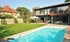 Ein modernes Haus mit großen Fenstern, einem Schwimmbad und einer Terrasse, umgeben von einem grünen Rasen.