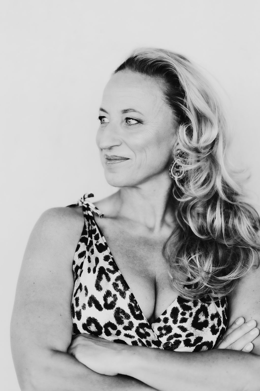 Schwarz-Weiß-Porträt einer Frau mit Leopardendruck-Top, die zur Seite blickt und die Arme verschränkt hat.
