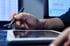 Eine Hand hält einen Stift über einem weißen Tablet mit dunklem Bildschirm.